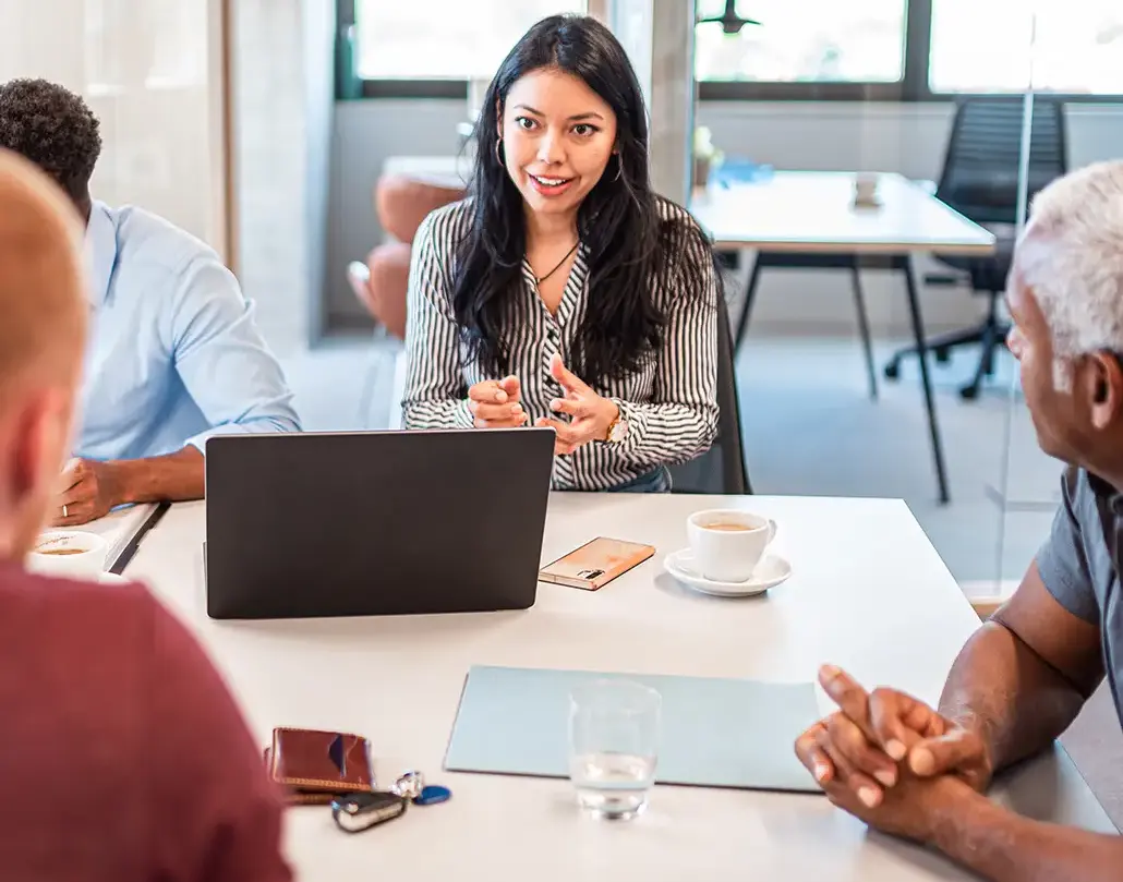 Group of business professionals in a meeting discussing ERP solutions, with a laptop and documents on the table, representing expert NetSuite consultants providing strategic guidance.